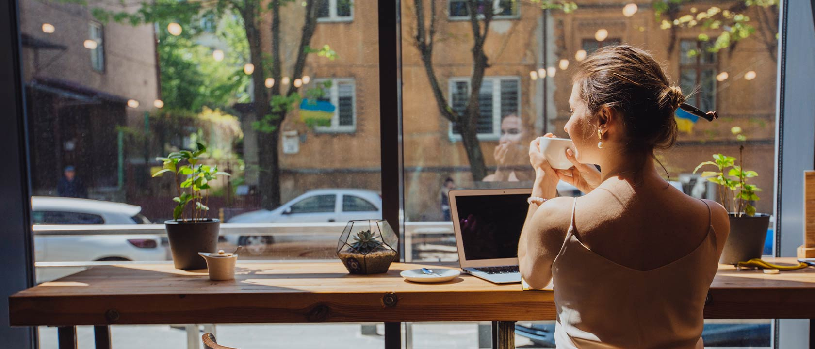 Junge Frau sitzt am Fenster in einem Café und arbeitet.